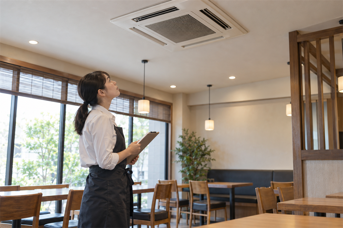 業務用エアコンの吸込口と吹出口を外から確認する店舗スタッフ