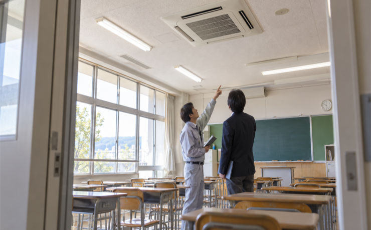 学校の教室で業務用エアコン交換について話す施設担当者と技術者