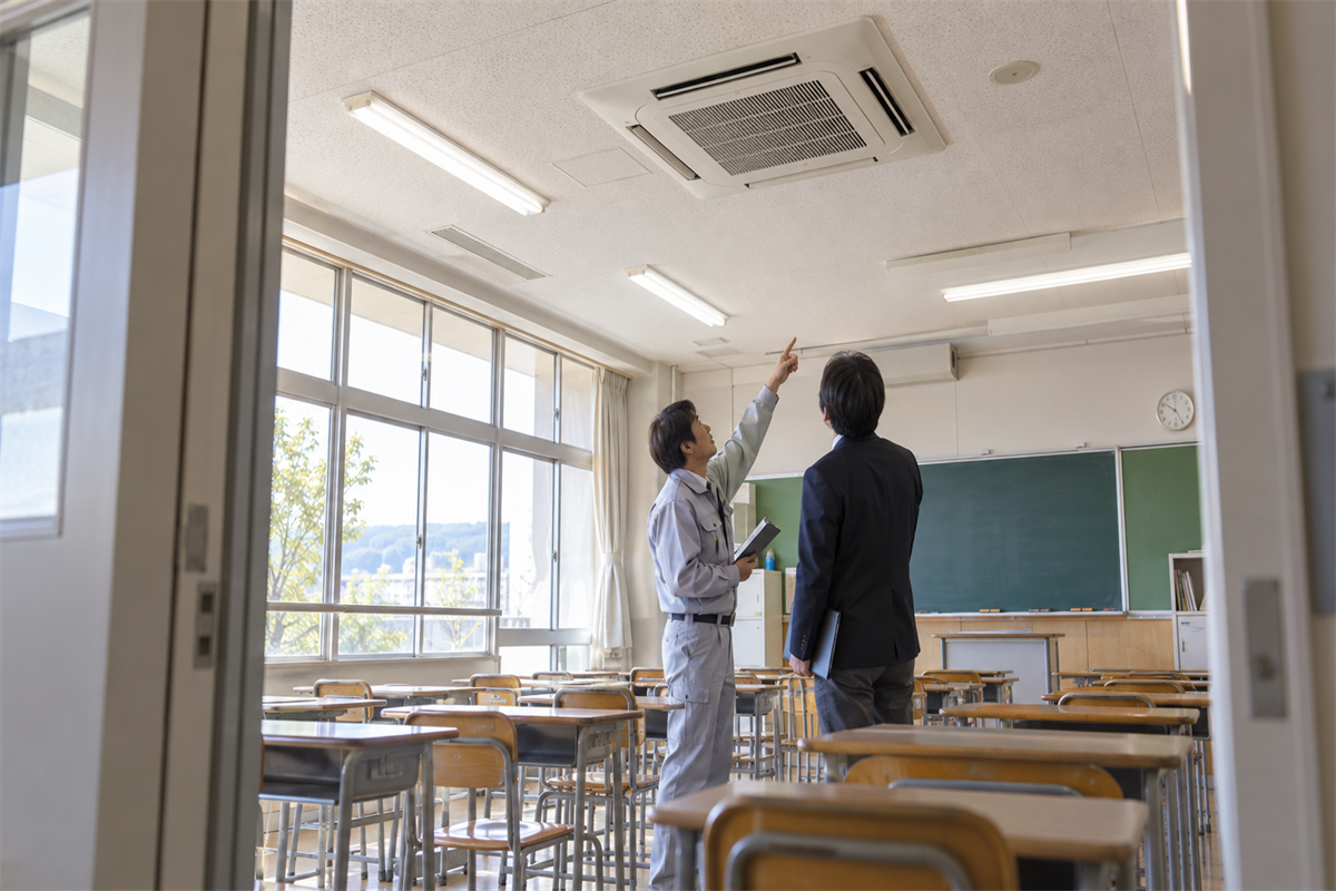 学校の教室で業務用エアコン交換について話す施設担当者と技術者